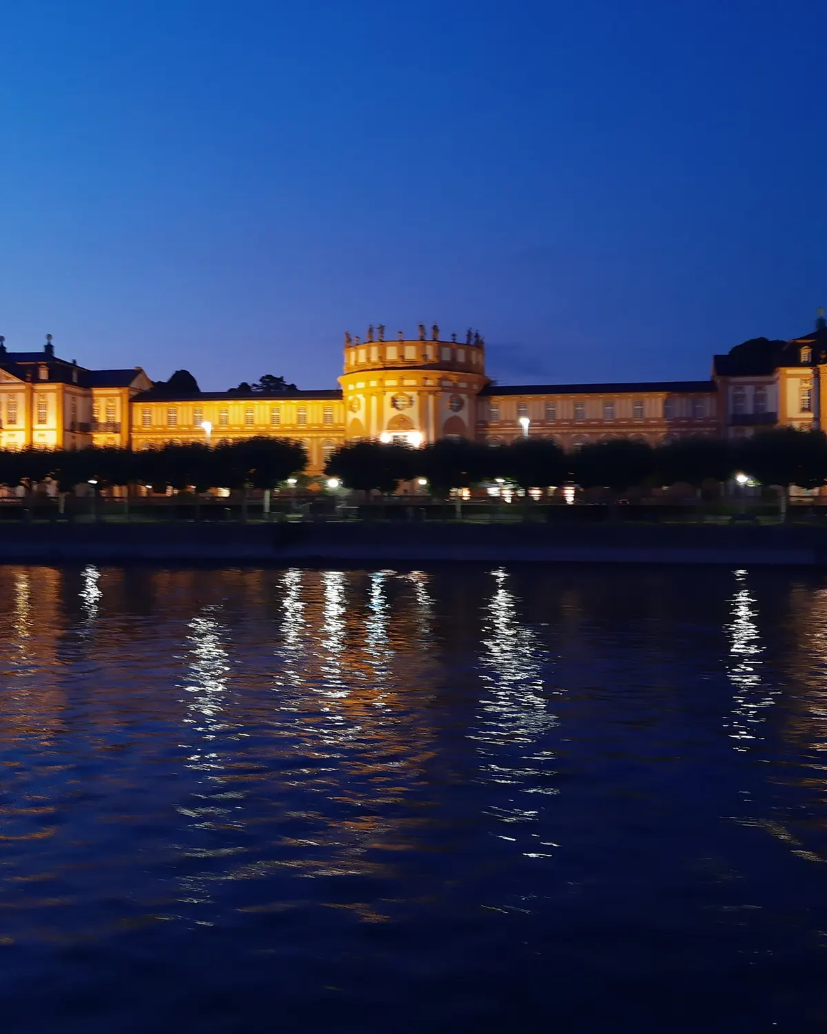 Schloss Biebrich zur blauen Stunde, vom Rhein aus gesehen, die beleuchtete Fassade spiegelt sich im Wasser